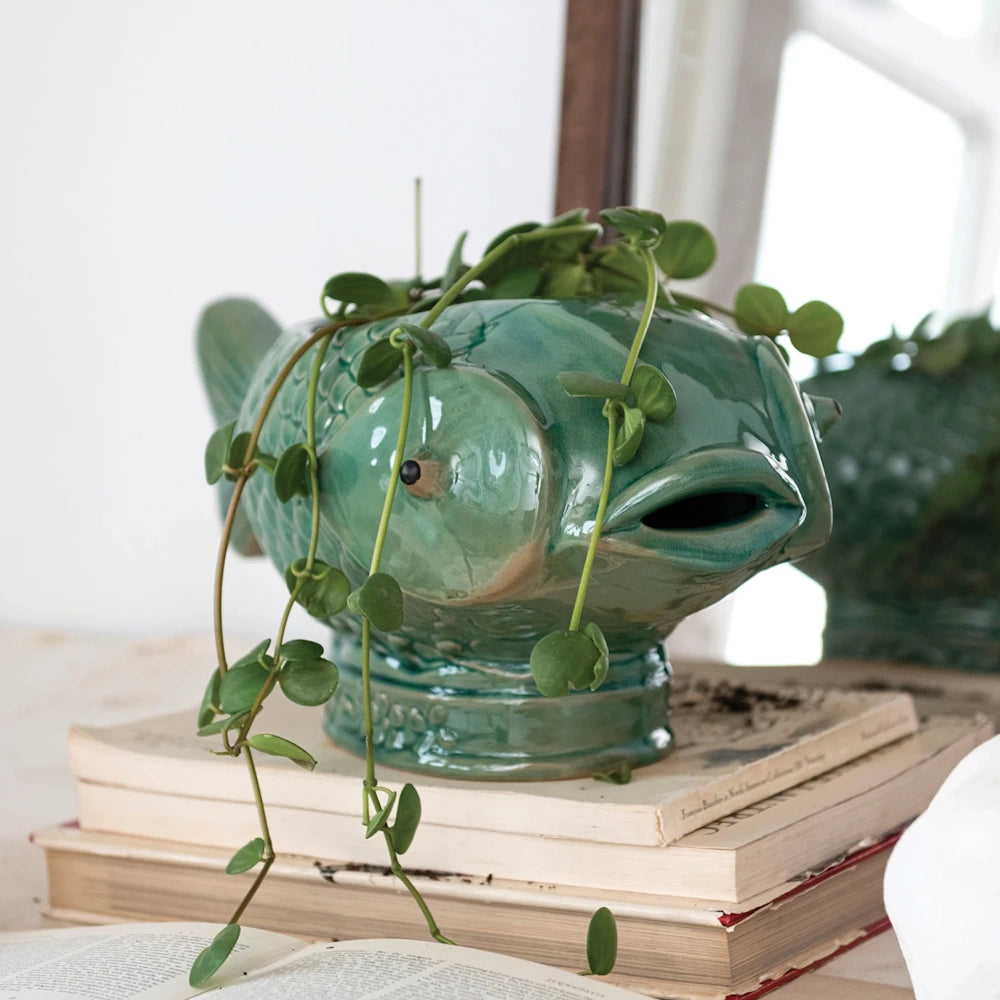 Green debossed stoneware fish planter with trailing vine plant on a stack of vintage books.