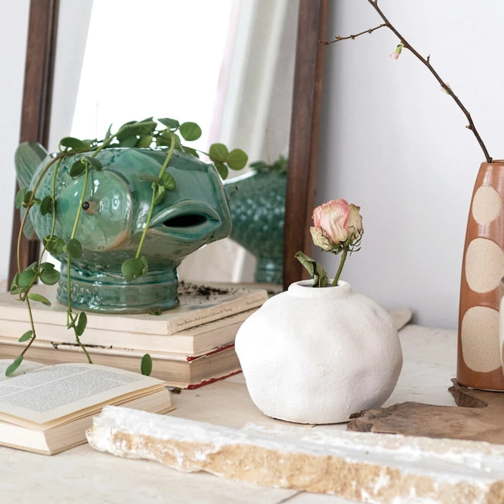 Green debossed stoneware fish planter with trailing vine plant on a stack of books next to a white textured bud vase.
