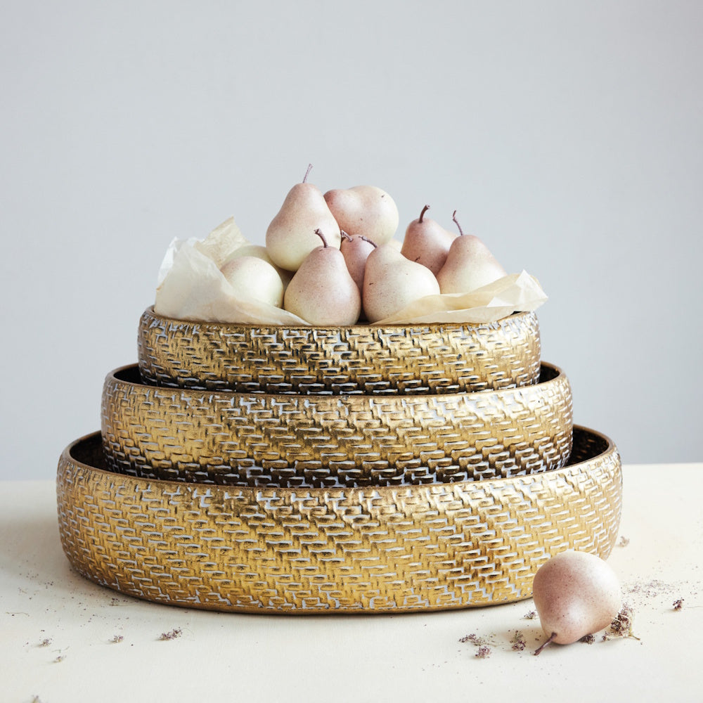 Stacked round gold woven metal trays filled with fresh pears resting on parchment paper.