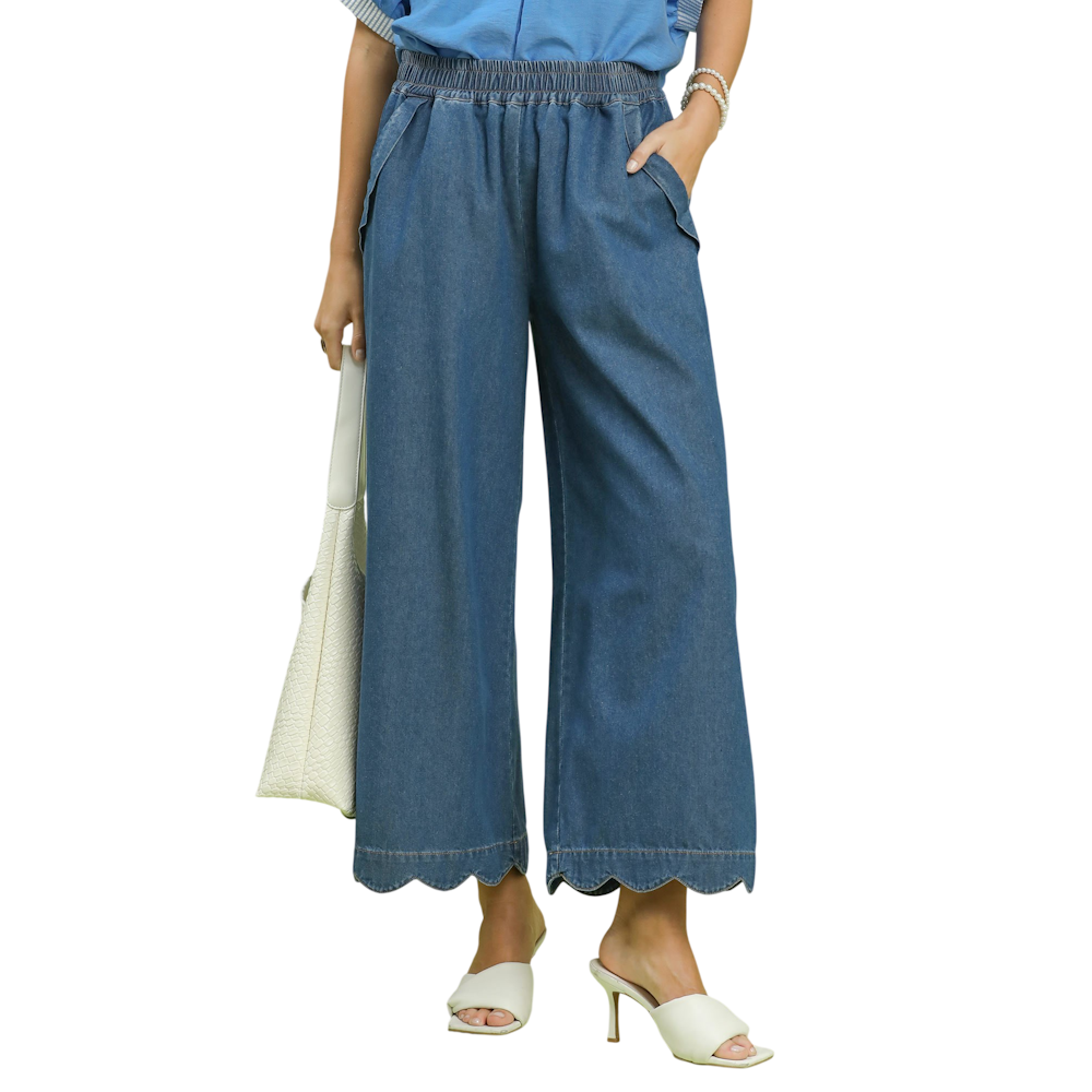 A person wearing wide-leg denim chambray pants with a scalloped hem, white heels, and a white handbag.