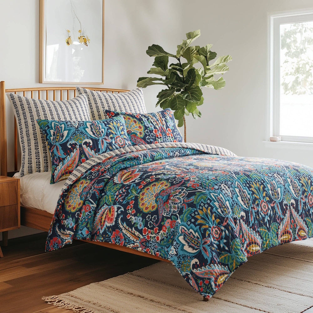 Bed styled with a colorful paisley quilt and matching shams, set against a wooden frame in a bright bedroom.