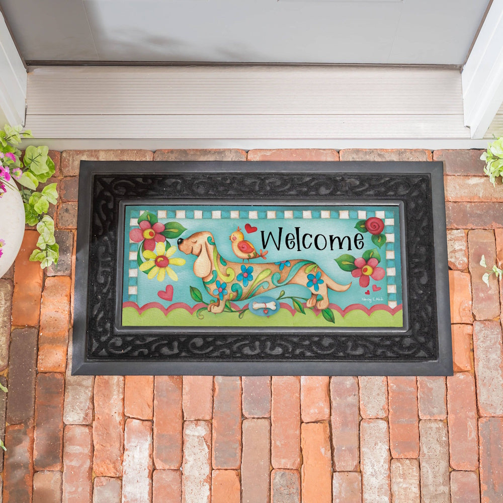 Colorful welcome doormat featuring a floral dachshund dog and a bird on a brick entryway.