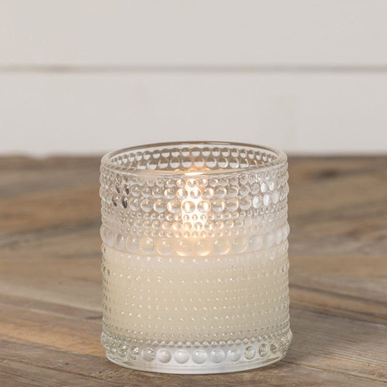 Clear dotted glass votive containing a glowing white 3D flameless candle on a wooden table.