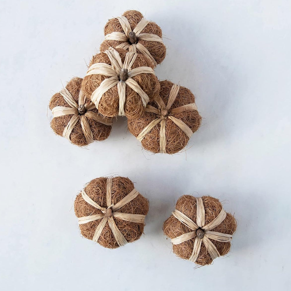 Top view of small rustic pumpkins made of natural brown coco fiber wrapped with raffia ties on white.