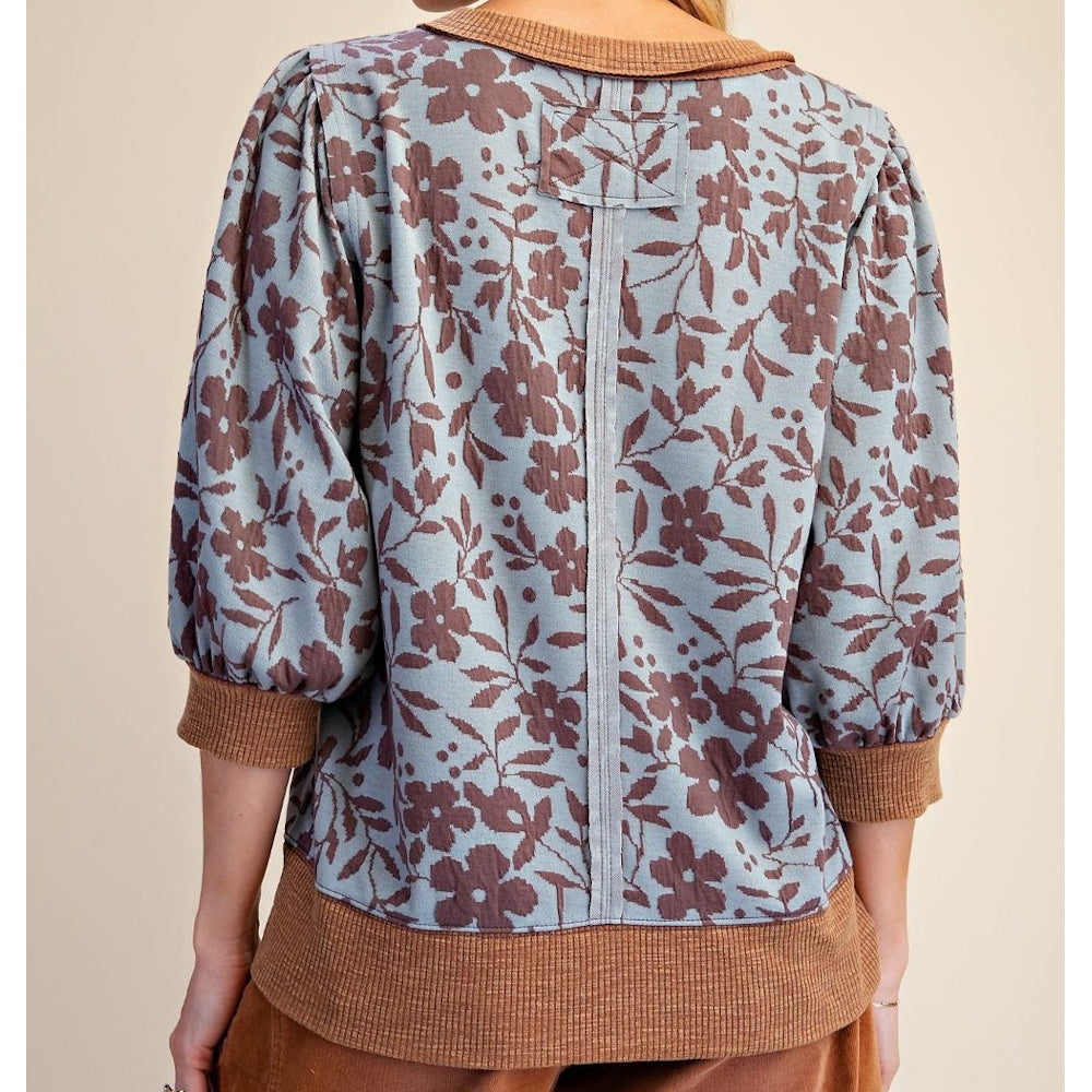 Back view of dusty blue floral knit top with brown ribbed trim and exposed back seam detailing.