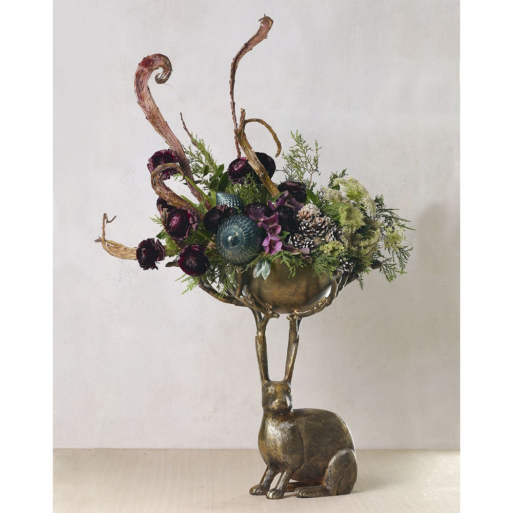 Side view of the antique gold rabbit bowl filled with deep purple flowers, pinecones, and decorative branches.