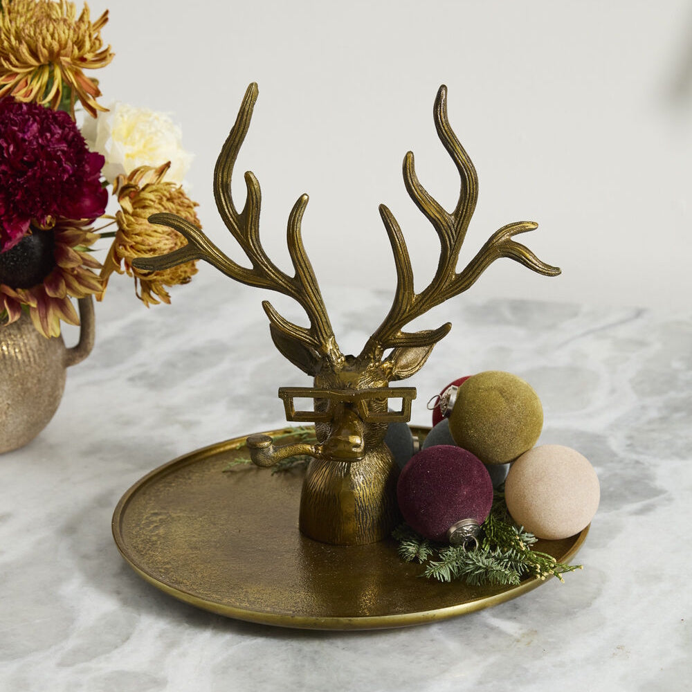Bronze deer tray with glasses and a pipe, decorated with velvet ornaments on a table.