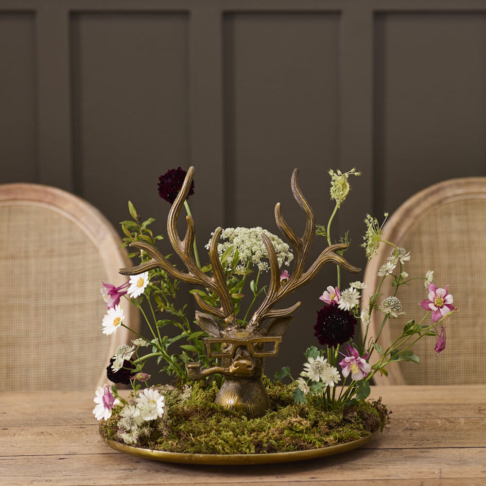 Bronze deer tray featuring a head with glasses and a pipe, styled with moss and flowers.