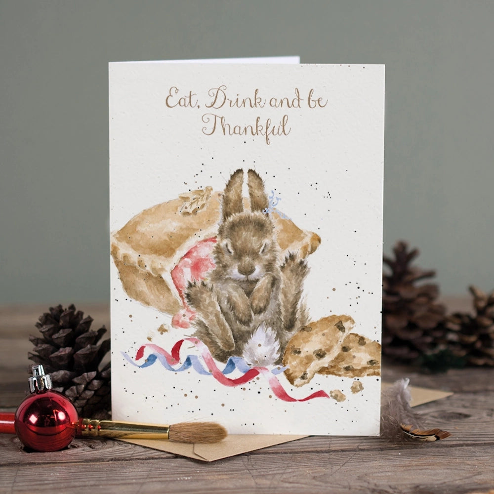 Greeting card with a bunny, pie, and "Eat, Drink and be Thankful" text surrounded by holiday decor.