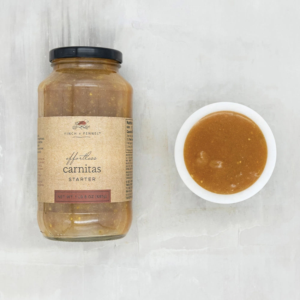 A jar of Finch + Fennel Effortless Carnitas Starter next to a small white bowl filled with the savory brown sauce.