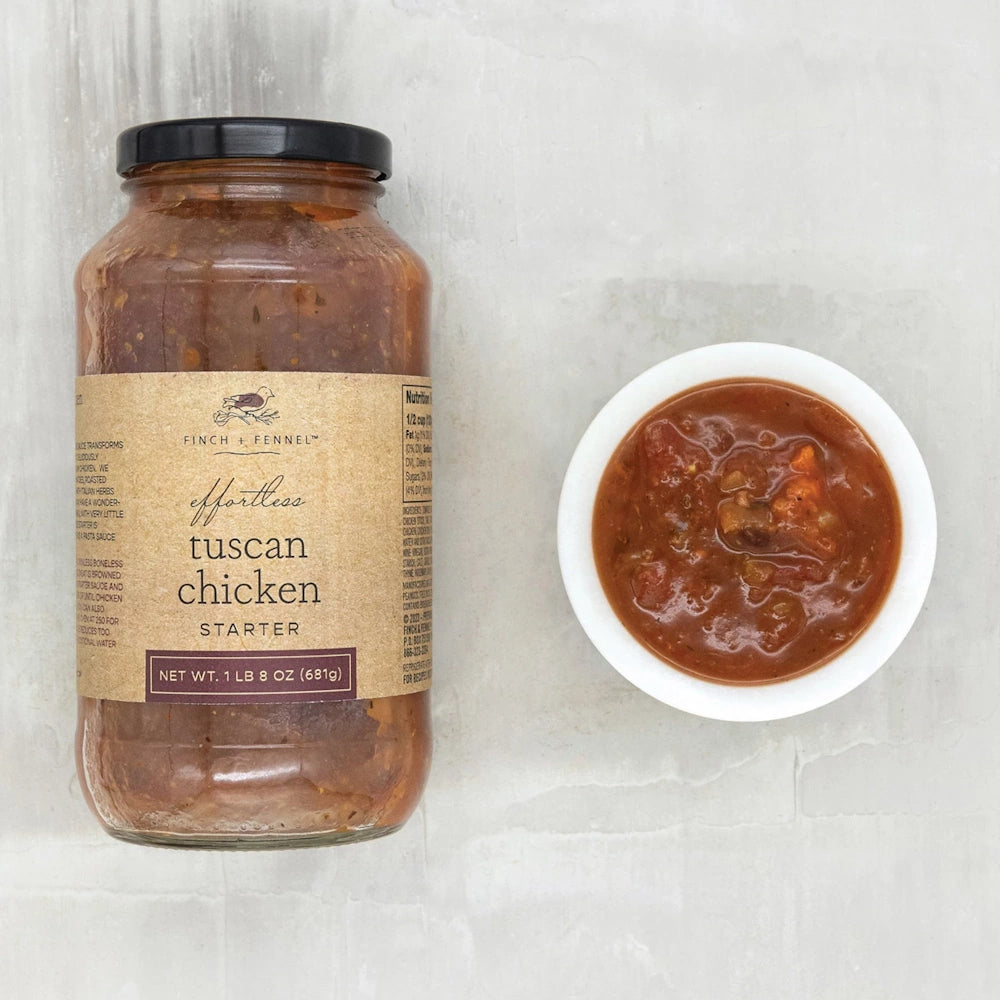 A jar of Finch + Fennel Effortless Tuscan Chicken Starter next to a small white bowl of the chunky tomato-based sauce.