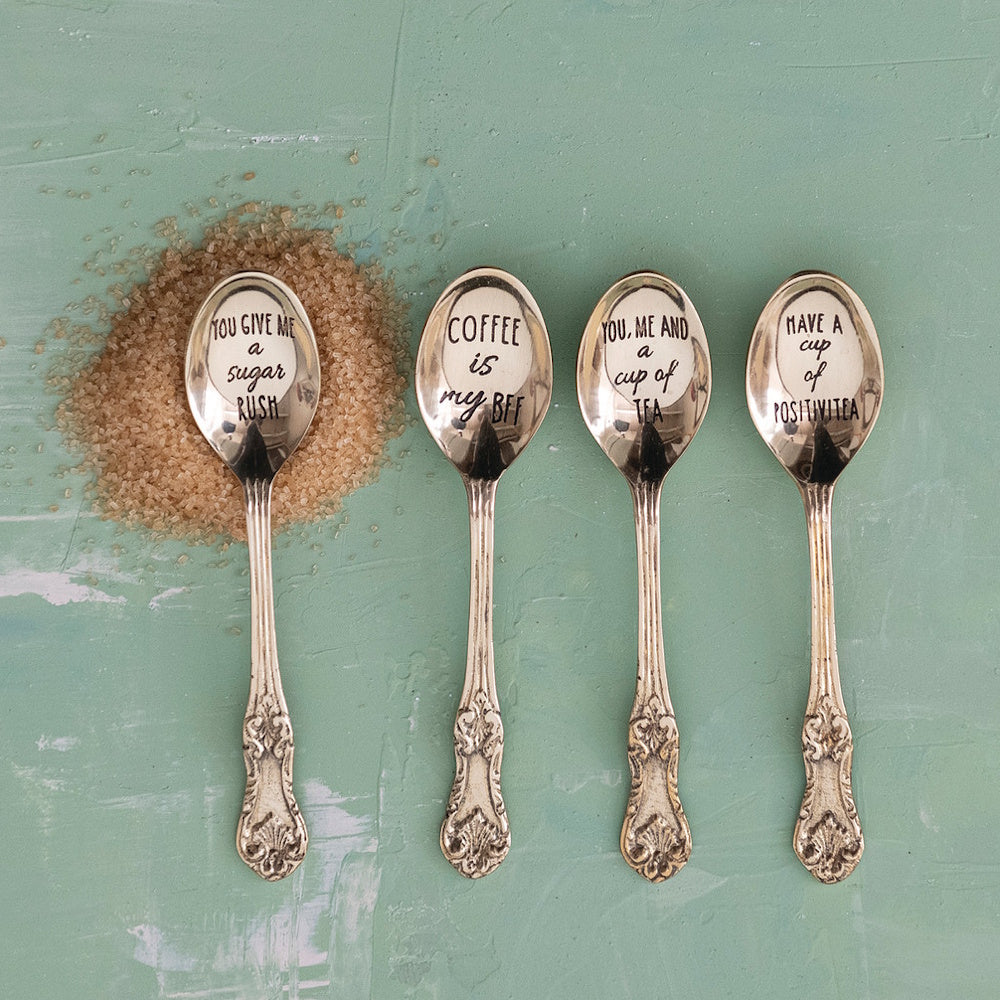 Four vintage brass spoons with etched coffee and tea sayings on a green background.