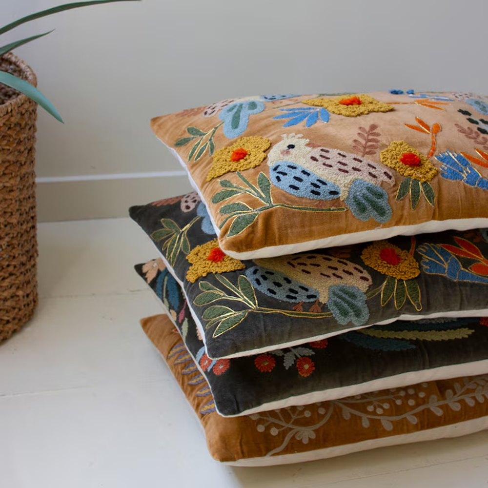 Stack of four embroidered velvet throw pillows with colorful floral and bird designs.