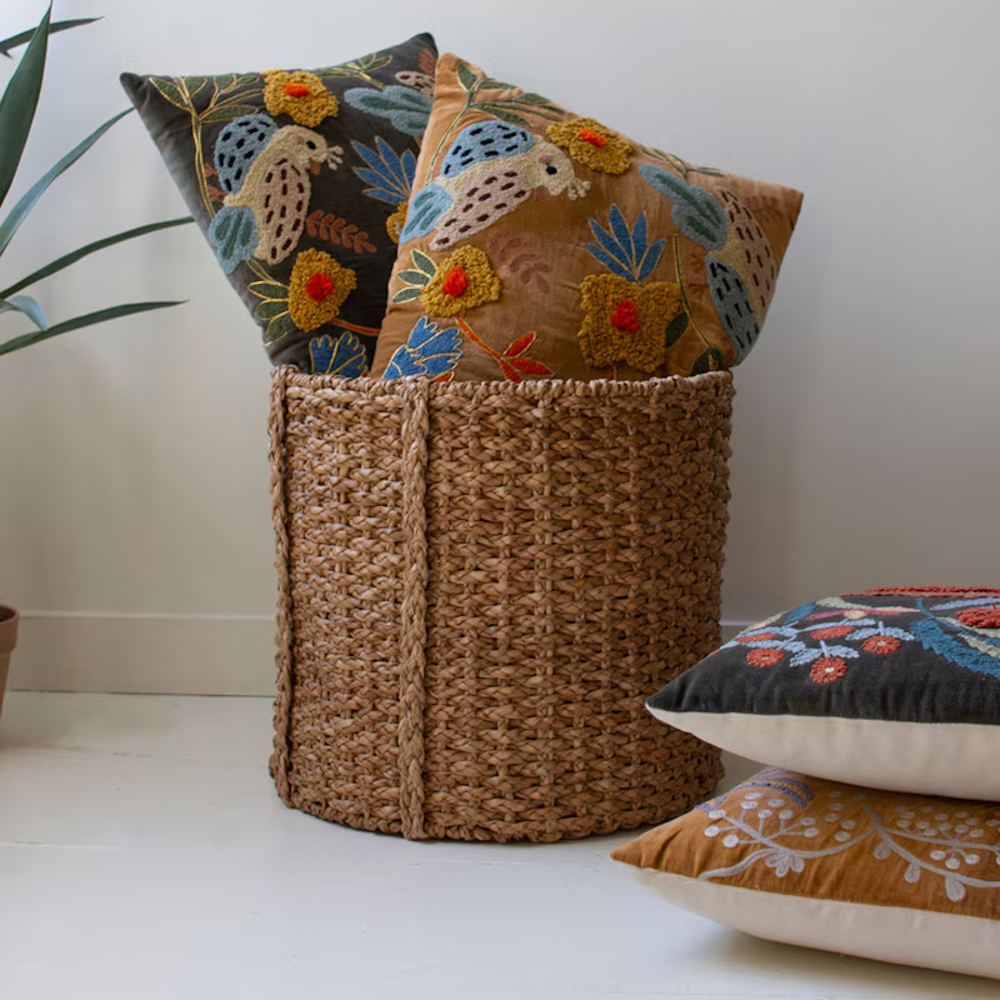 Embroidered velvet throw pillows styled in and next to a woven storage basket.