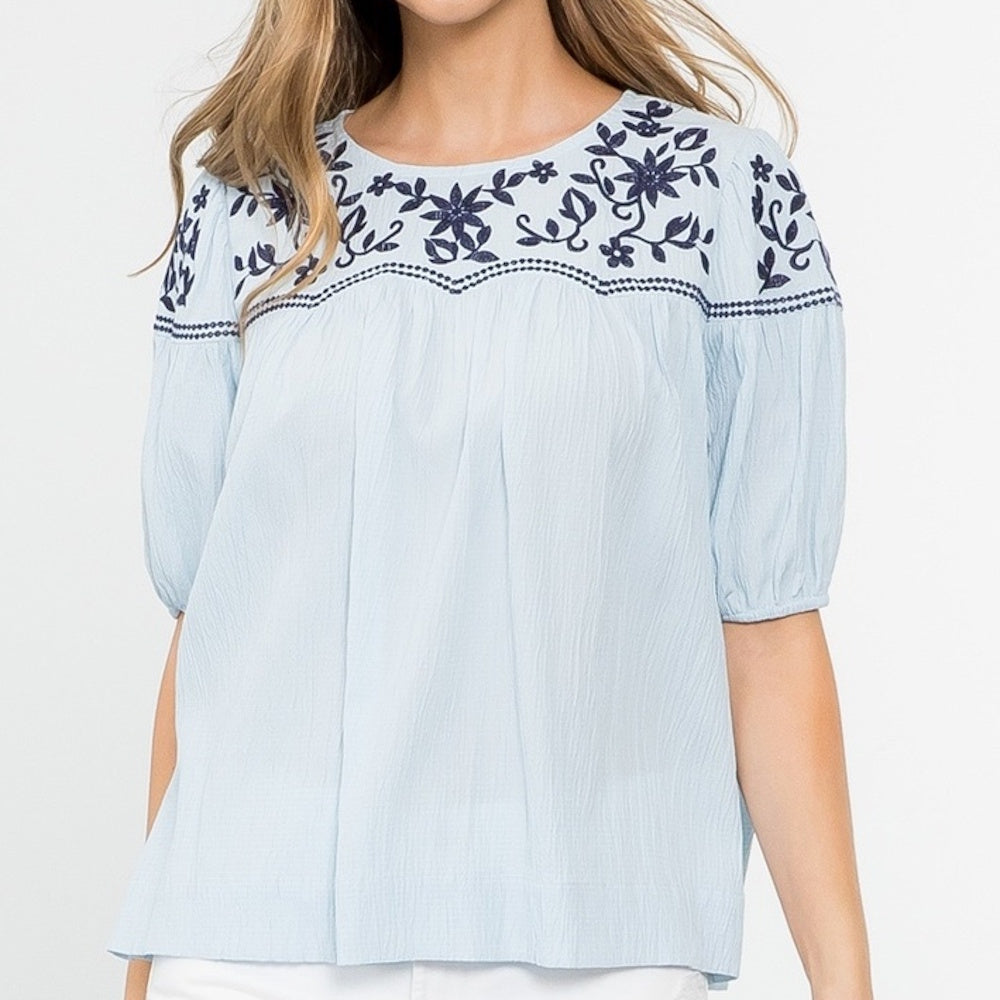 Light blue short-sleeve top with navy blue floral embroidery along the neckline and shoulders.