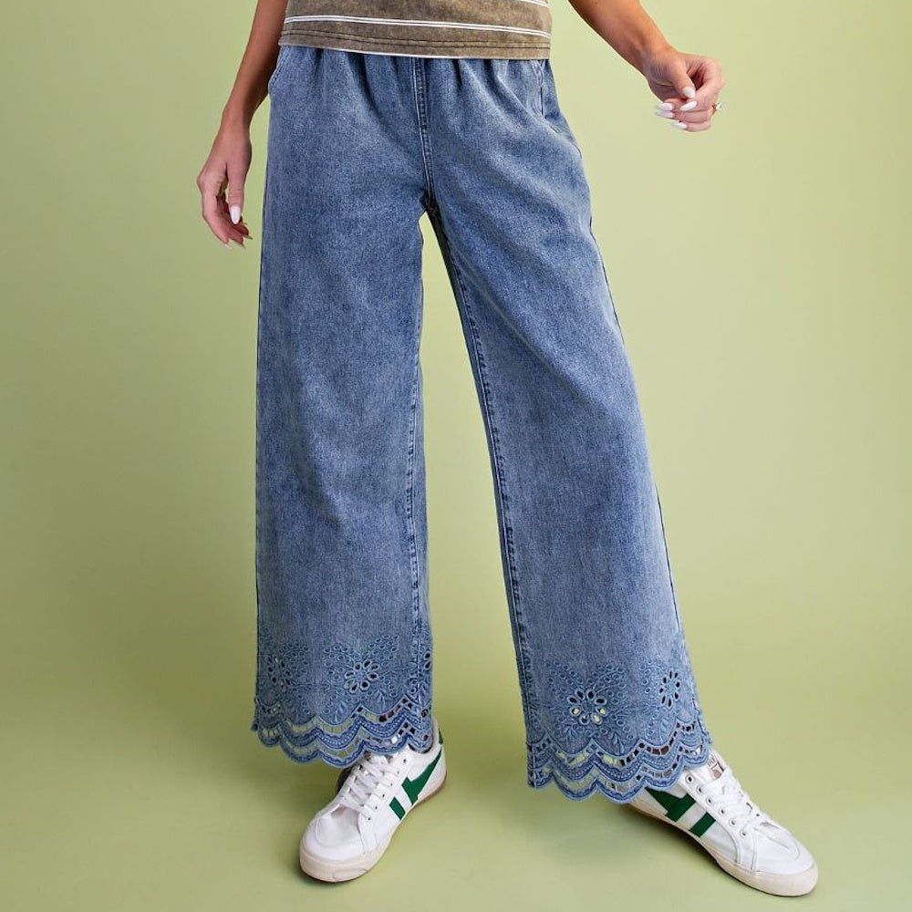 Wide-leg washed blue denim pants with embroidered eyelet lace hem paired with white sneakers.
