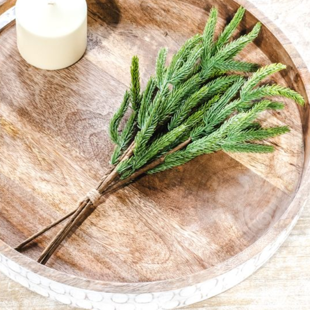 Artificial evergreen pine stem bundle tied with twine, placed on a round wooden tray with a candle.