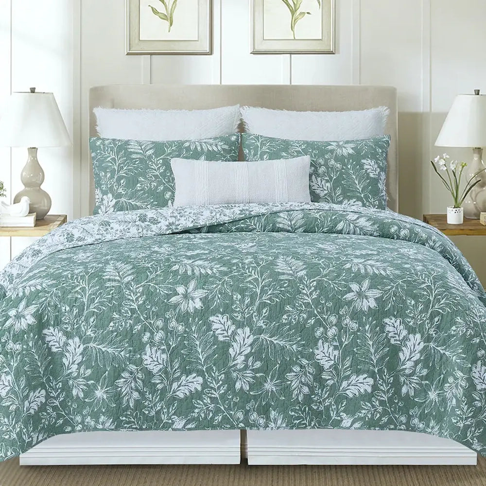 Green and white floral botanical quilt and matching pillows on a bed in a bright, neutral bedroom.