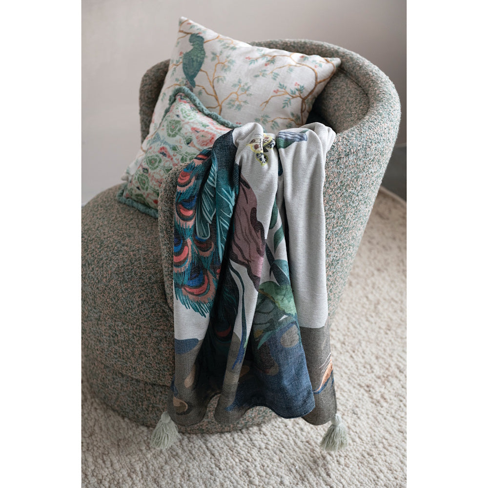 Fabric blend chenille throw featuring a peacock design draped over a textured armchair with pillows.