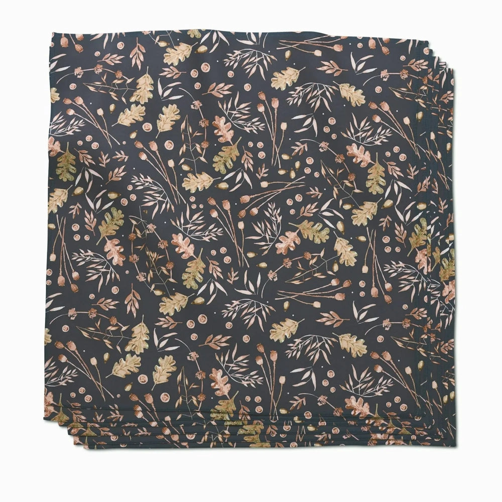 A stack of dark gray dinner napkins featuring an autumnal pattern of oak leaves, acorns, and seed pods.