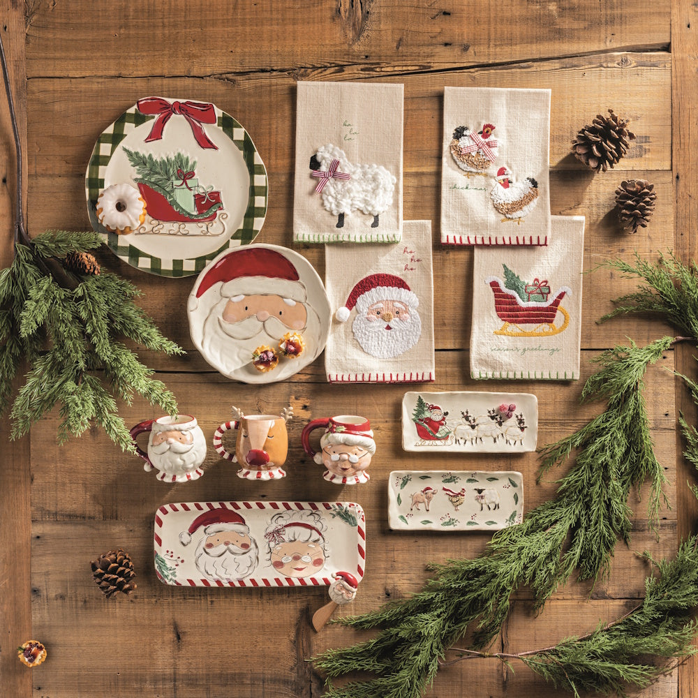 Christmas display with platters, plates, towels, mugs, and pinecones on a wooden table.