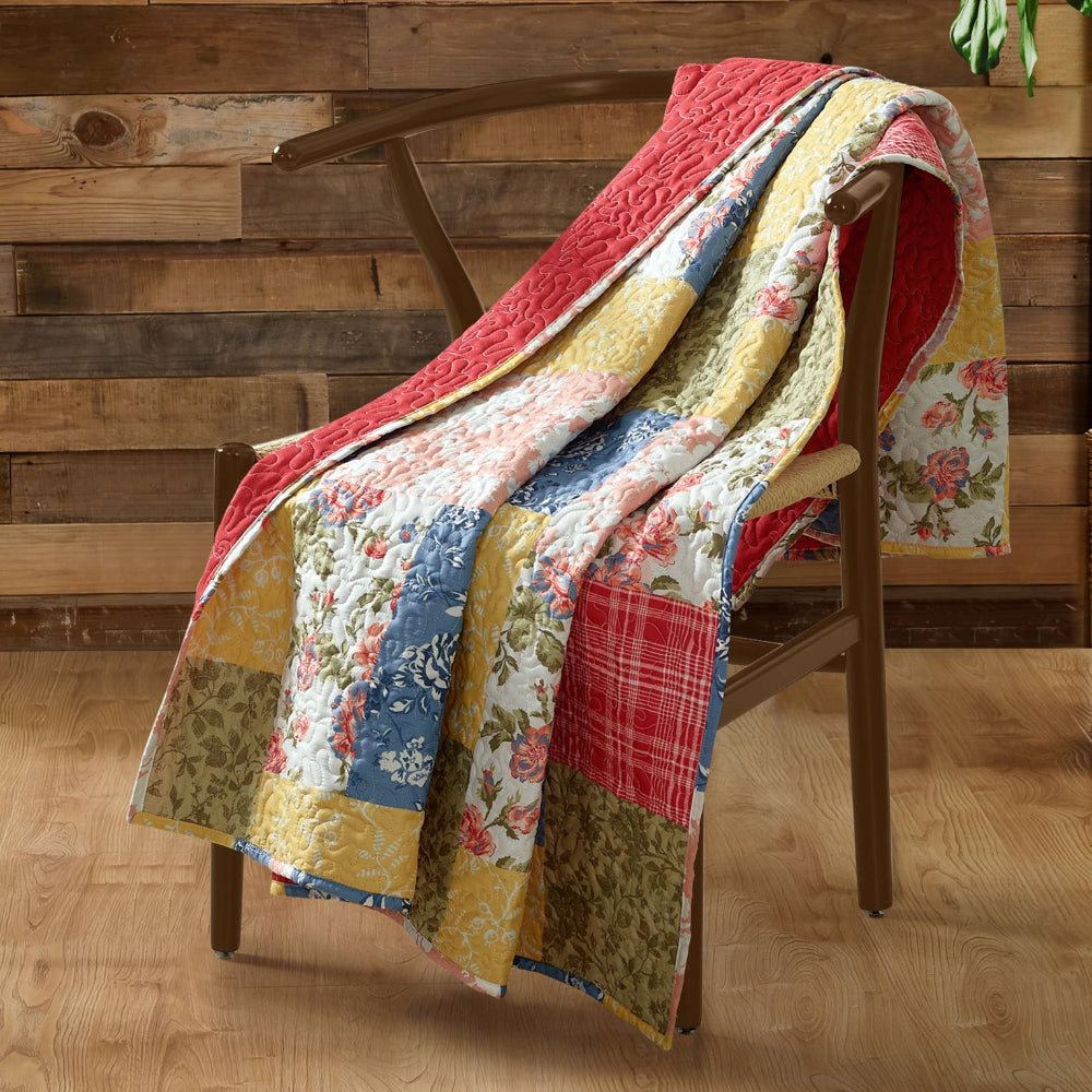 Colorful patchwork floral quilt draped over a wooden chair in a farmhouse-style room with wood paneled walls.