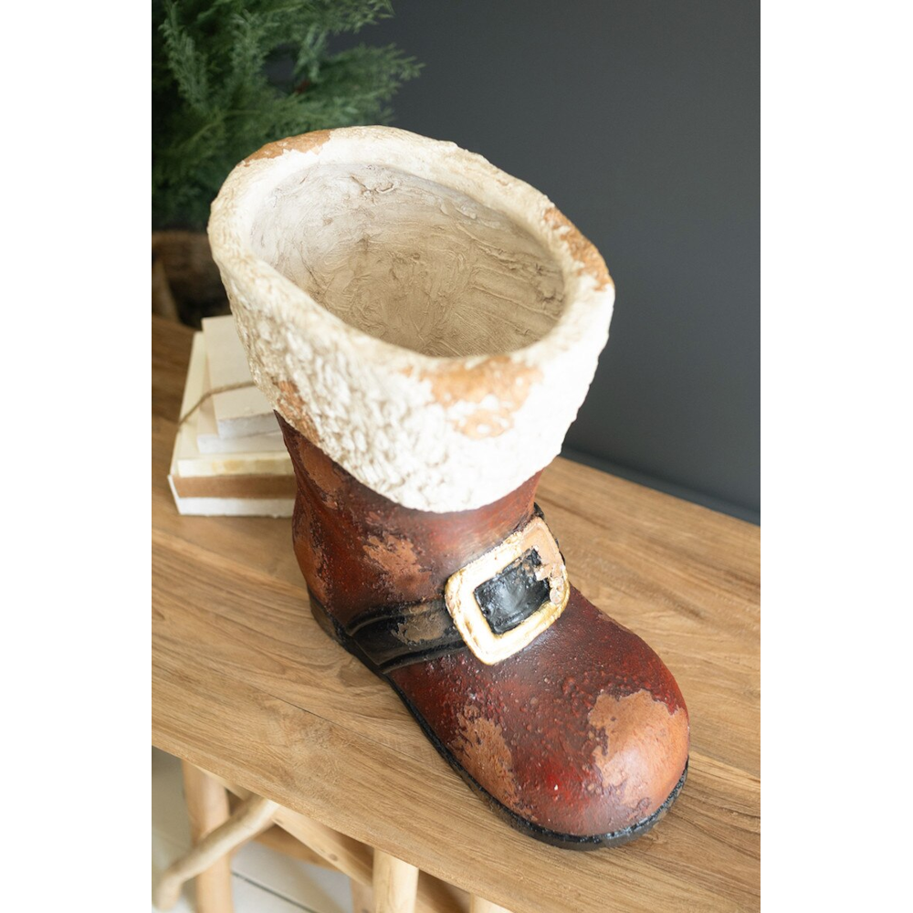 Top-down view of a hollow, rustic faux-concrete Santa boot container on a wooden table.