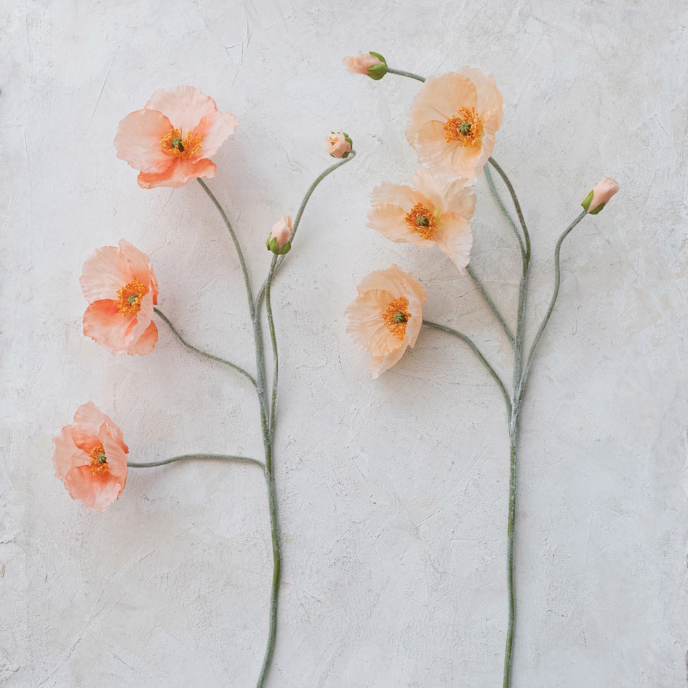 Delicate peach faux poppy flower stems with open blooms and buds against a textured light background.