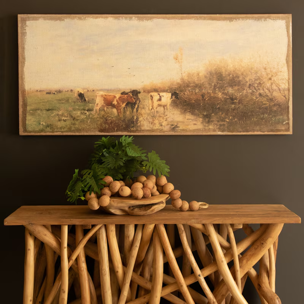 Panoramic canvas painting on burlap depicting cows in a field hanging above a rustic console table.