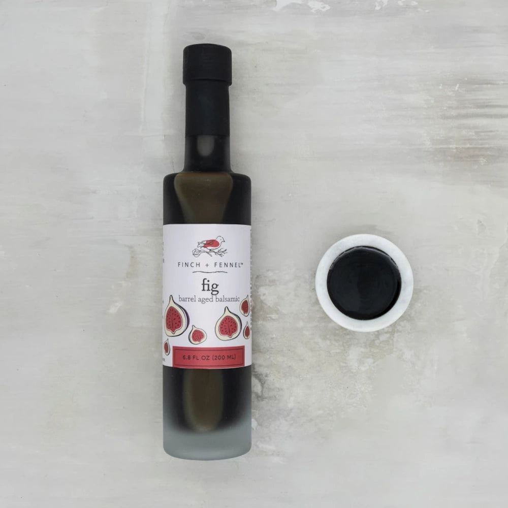 Finch + Fennel Fig Barrel Aged Balsamic Vinegar bottle next to a small white bowl of dark balsamic glaze.