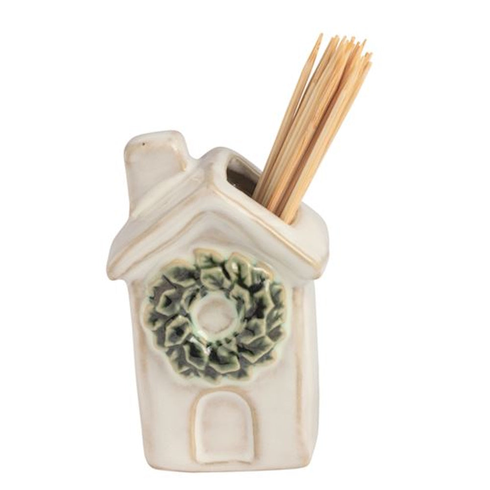White ceramic house-shaped toothpick caddy decorated with a green wreath, holding wooden toothpicks.