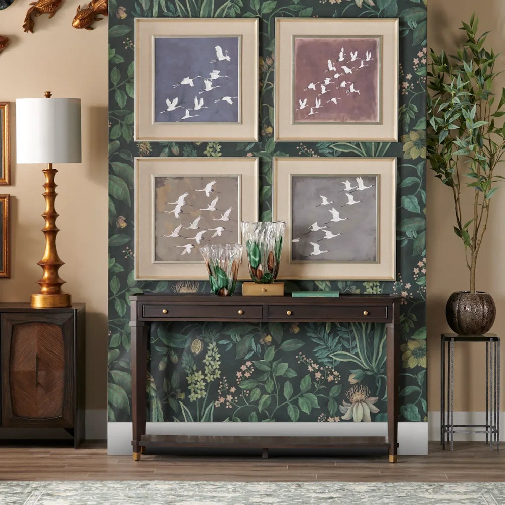 Four framed bird prints displayed above a console table against dark botanical wallpaper in a decorated room.