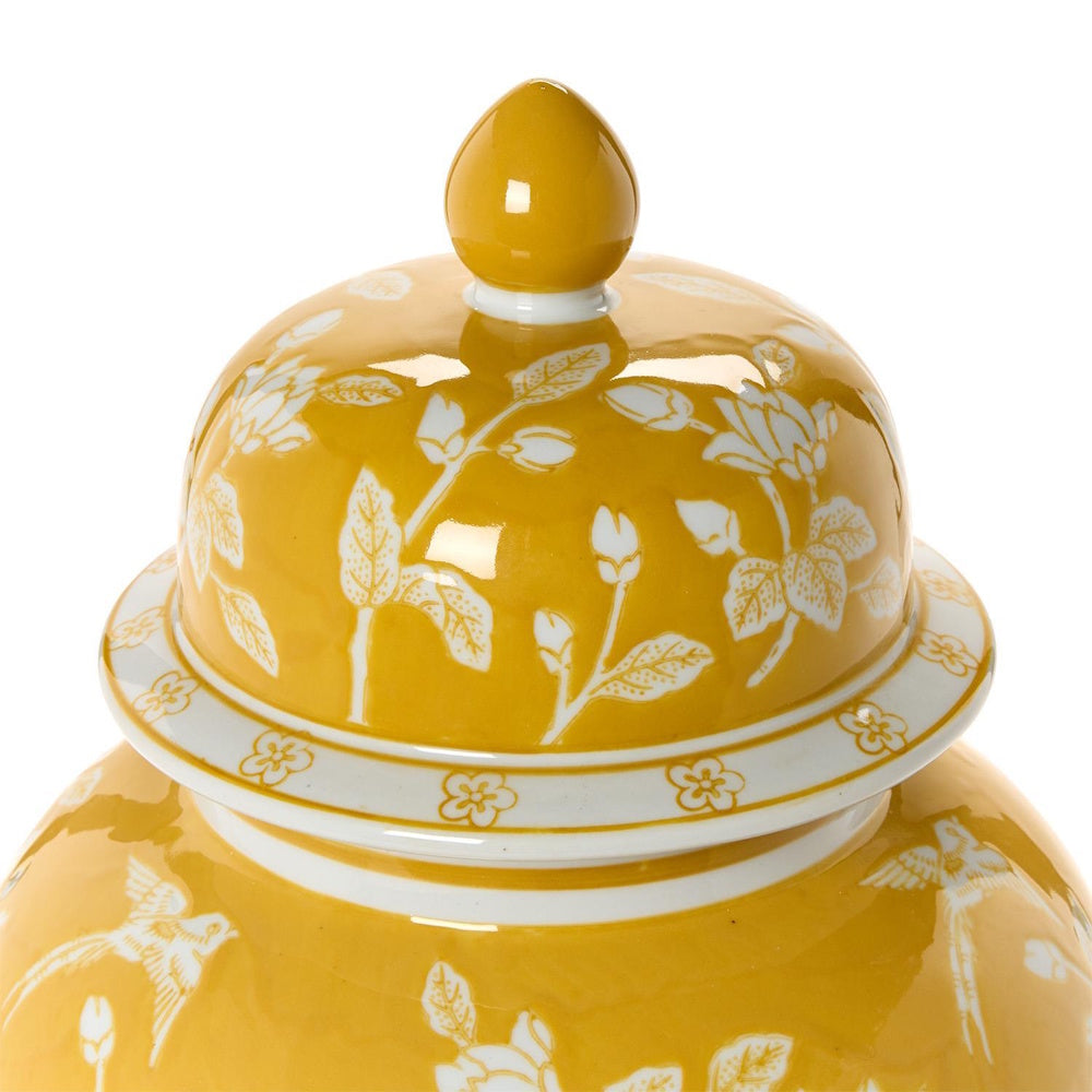 Yellow ceramic temple jar lid with white floral motifs and a pointed finial top.