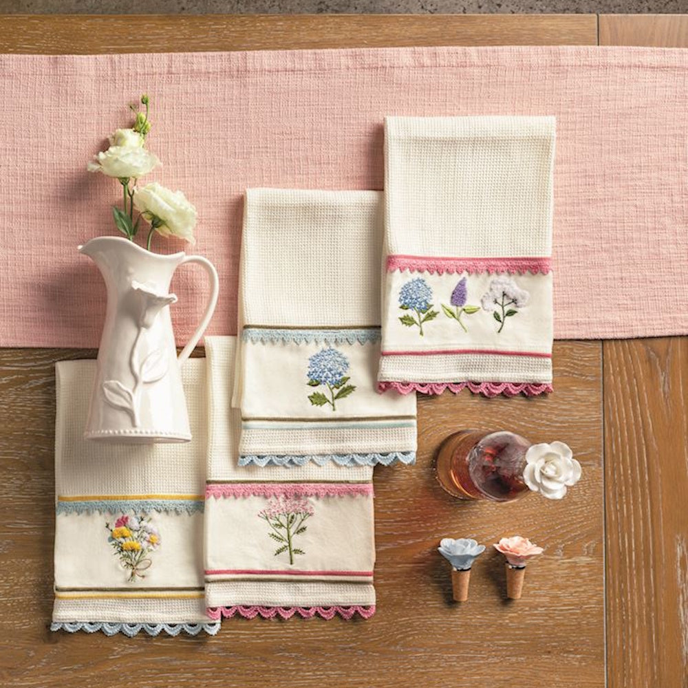 Floral embroidered waffle-knit hand towels with scalloped lace trim, displayed on a wooden table with spring decor.