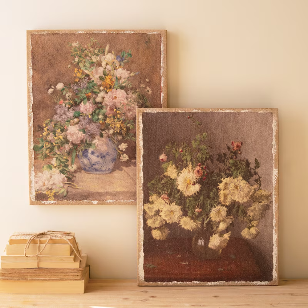 Two vintage floral canvas prints on burlap with distressed white borders leaning against a beige wall.