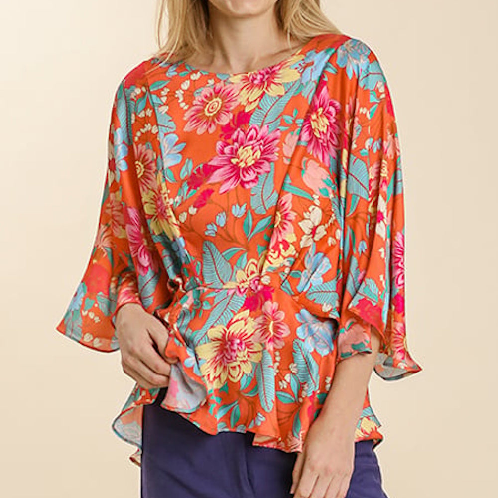 Woman wearing an orange round-neck top with a vibrant floral print, pleated front, and wide kimono sleeves.