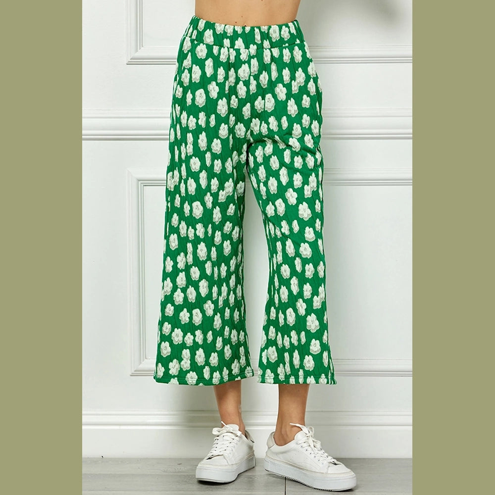 Cropped wide-leg green pants with a white floral pattern, paired with white sneakers.