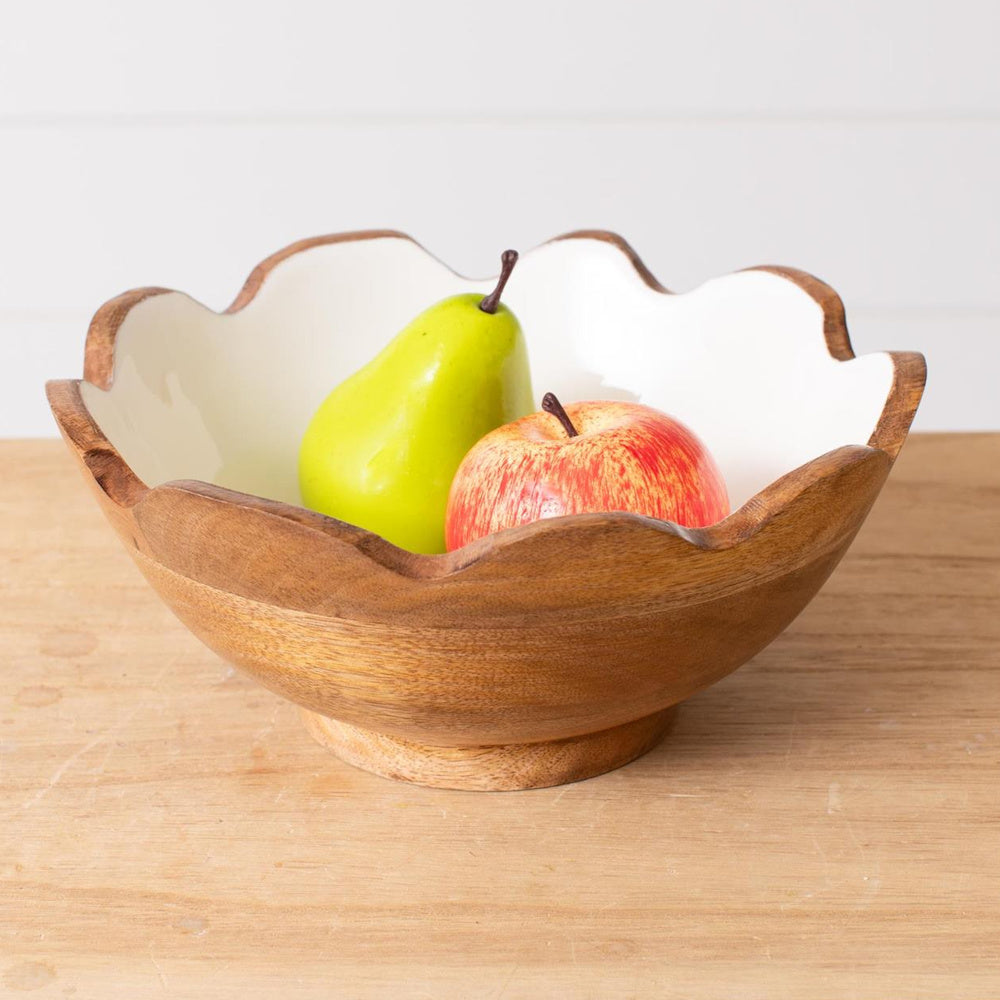 Fluted mango wood fruit bowl with white enamel interior holding a green pear and red apple on a wooden table.