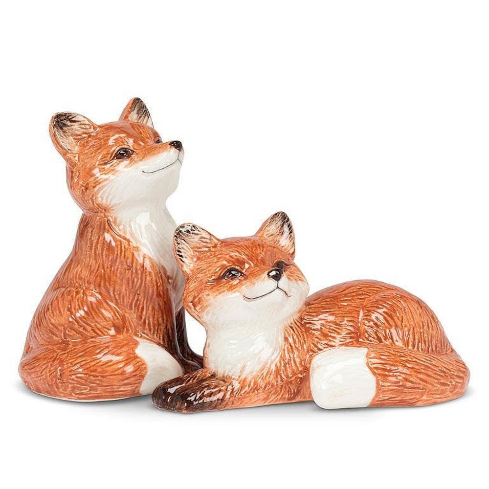 Pair of ceramic fox salt and pepper shakers, one sitting and one lying down, on a white background.