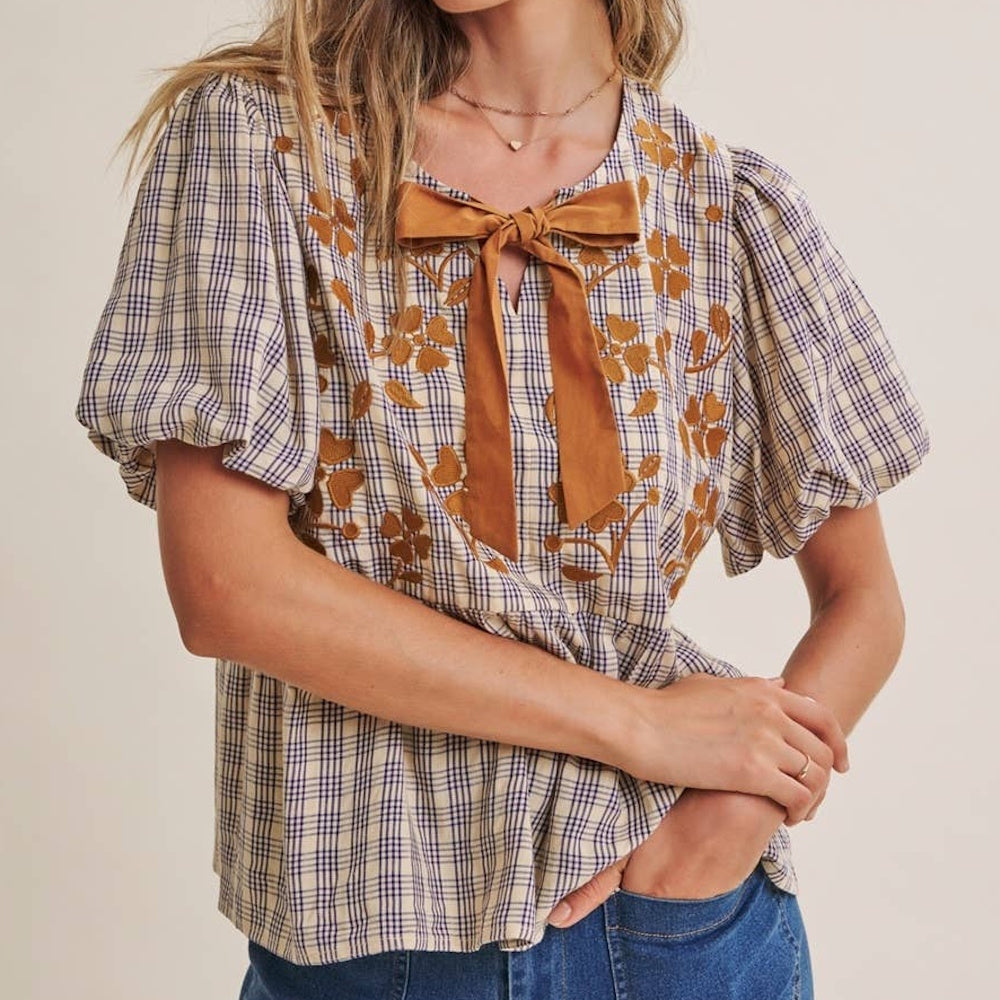 Plaid babydoll blouse with brown floral embroidery, puff sleeves, and a bow tie at the neckline.