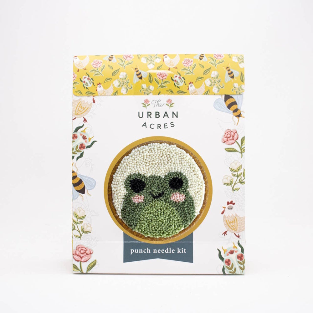 The Urban Acres punch needle kit packaging featuring a cute green frog design in a round frame.