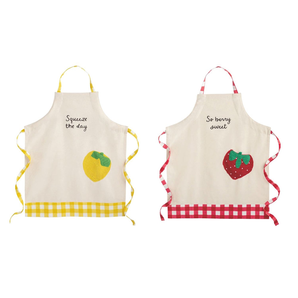 Two fruit-themed aprons with lemon and strawberry crochet pockets, pun text, and gingham trim on a white background.