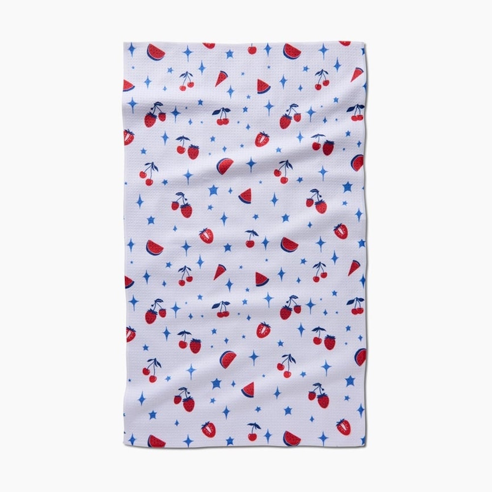 White towel featuring a repeating pattern of red summer fruits like cherries and blue stars.