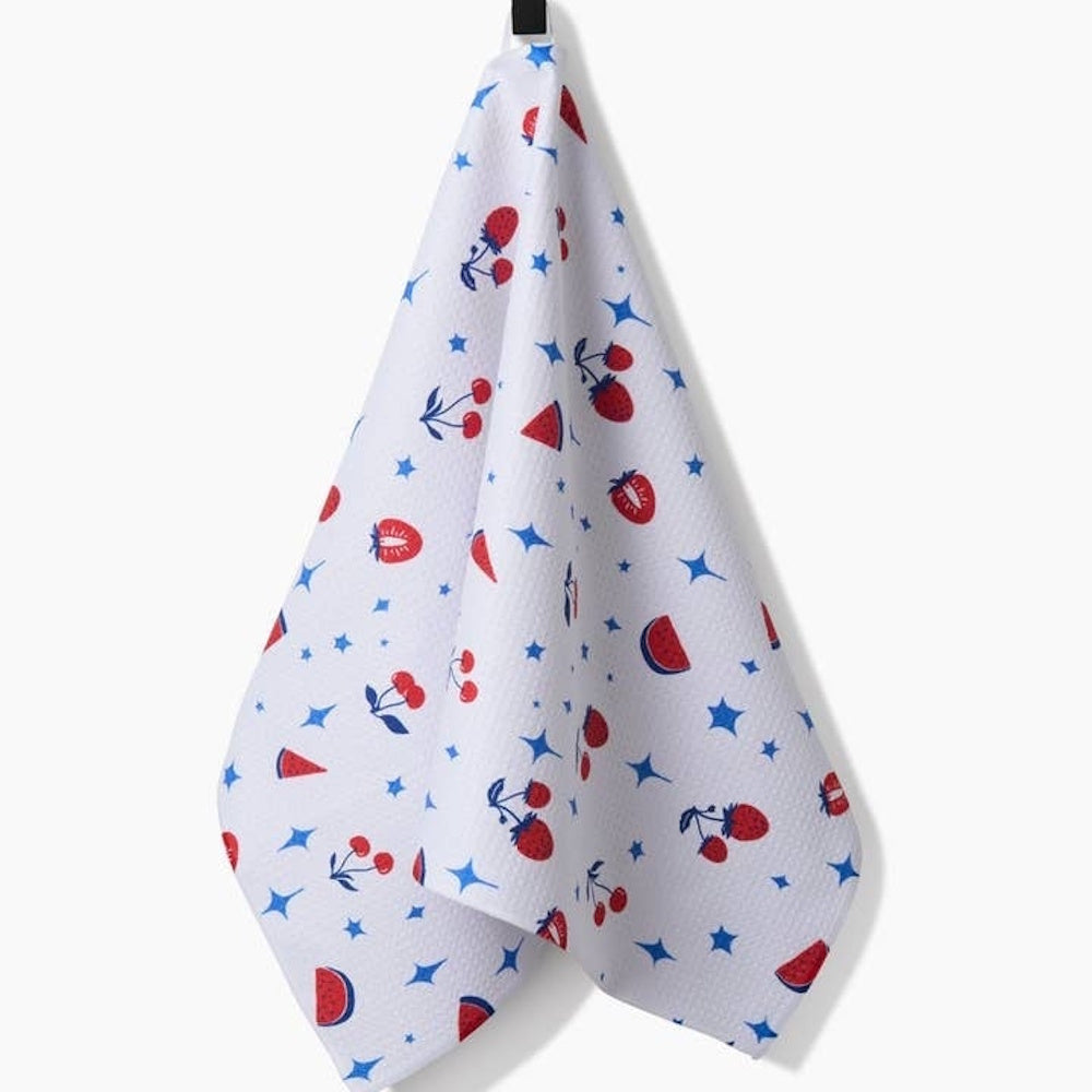 White kitchen towel patterned with red fruit (strawberries, cherries, watermelon slices) and blue stars.