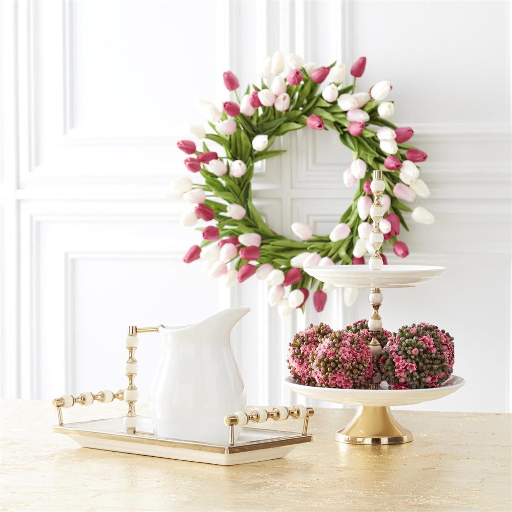 Fuchsia, pink, and white mini tulip wreath hanging behind a white pitcher and tiered server on a gold table.
