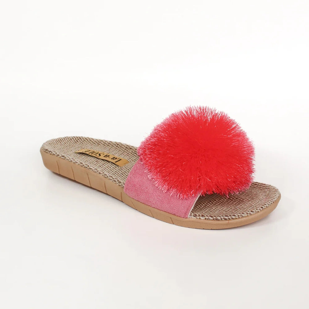 A pink slide sandal with a woven footbed and a large, fluffy bright pink pom-pom on the upper strap.