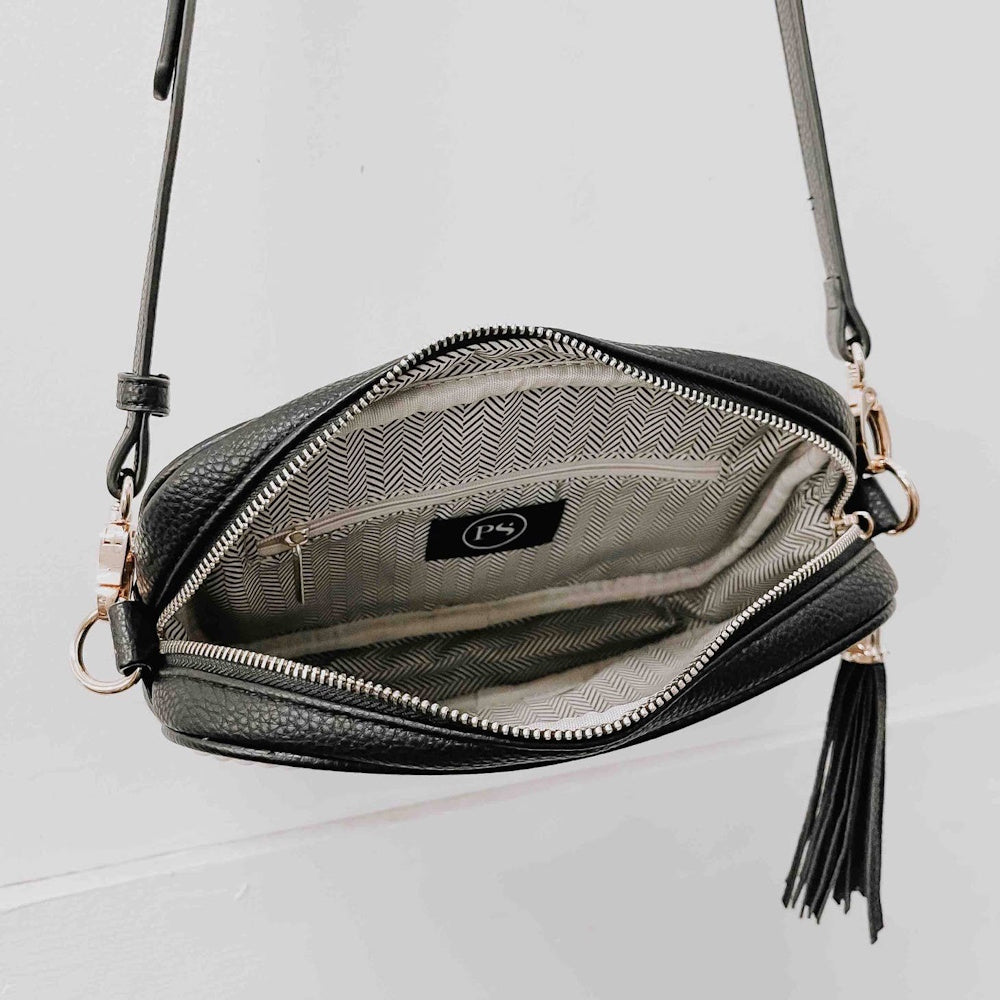 Open black crossbody bag showing its patterned interior, inner zipper pocket, and attached black tassel.