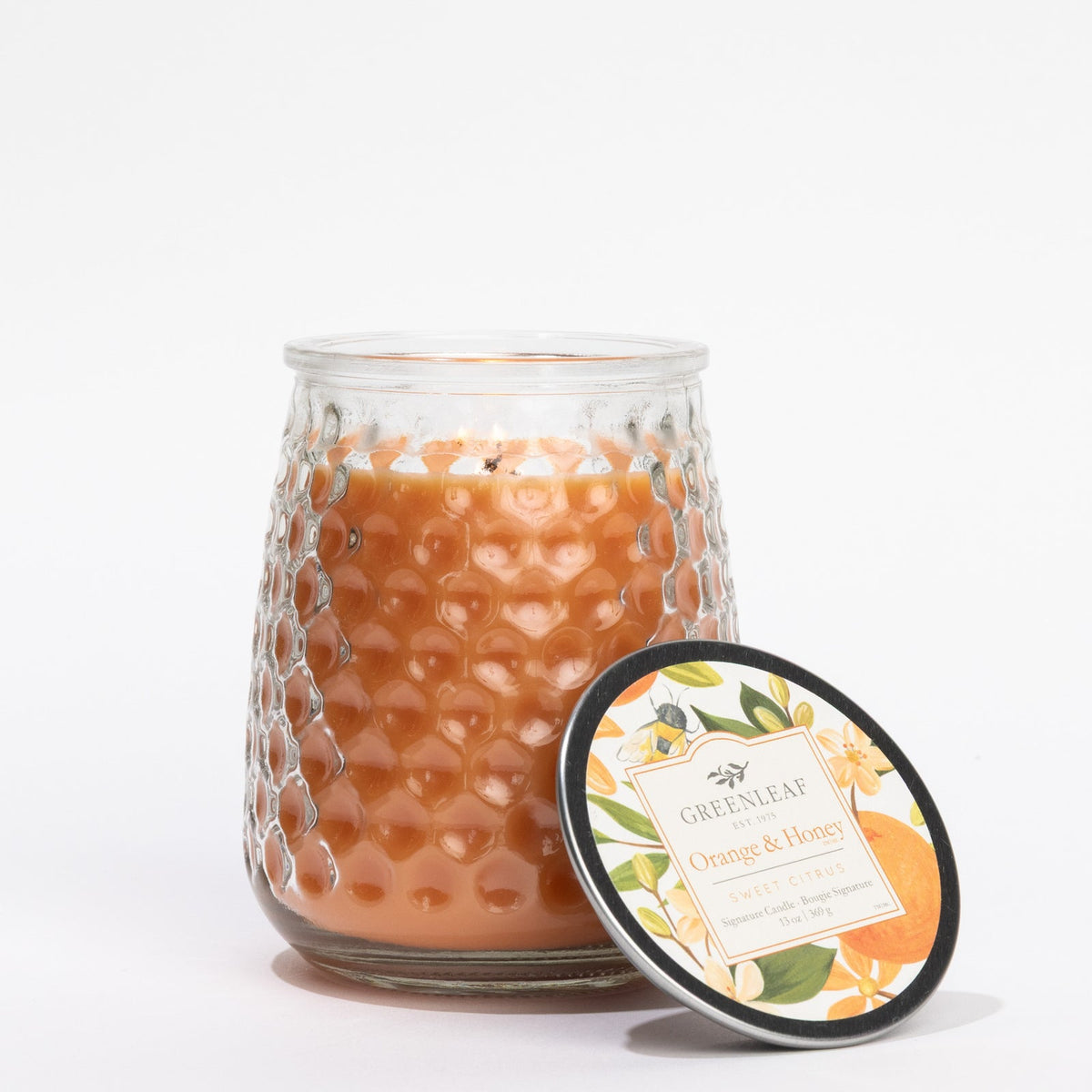 Glass candle with textured design and decorative lid on a white background