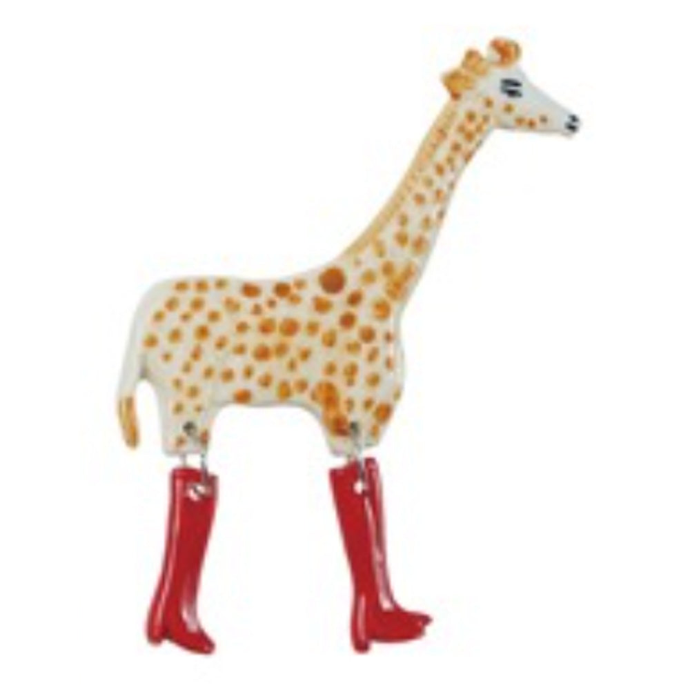 A giraffe-shaped stoneware magnet with orange spots and two dangling red-booted legs against a white background.