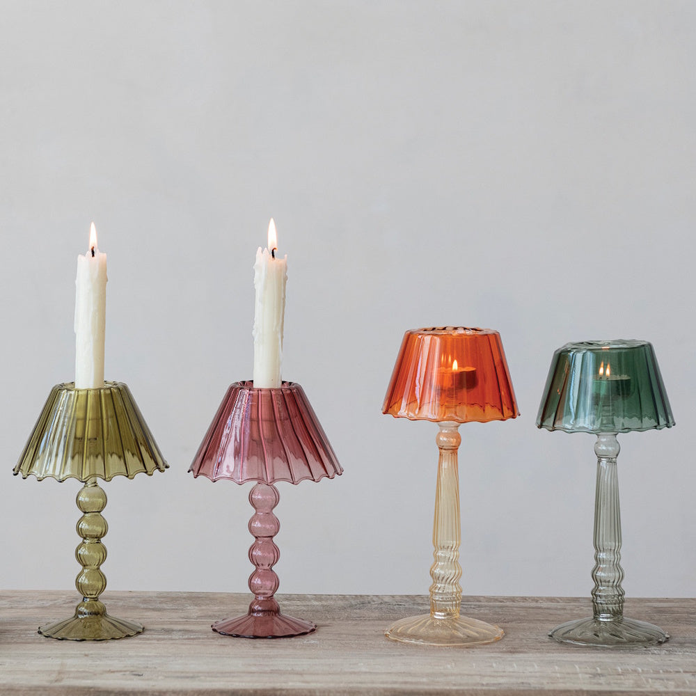 Four colored glass lampshade candle holders displaying lit taper candles and tealights.